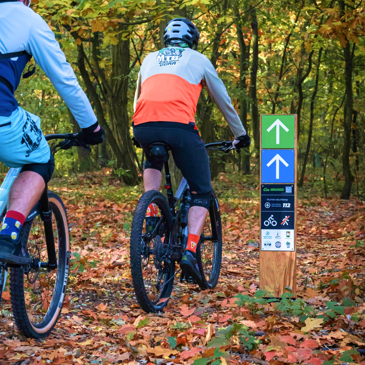 MTB bike riders from the MTB Zielona Góra group entering the Wzgórza Piastowskie Singletrack trail, passing by a post with the designed signage.